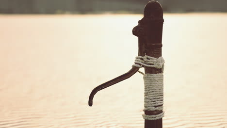 old hand pump by tranquil waters at sunset in rural area