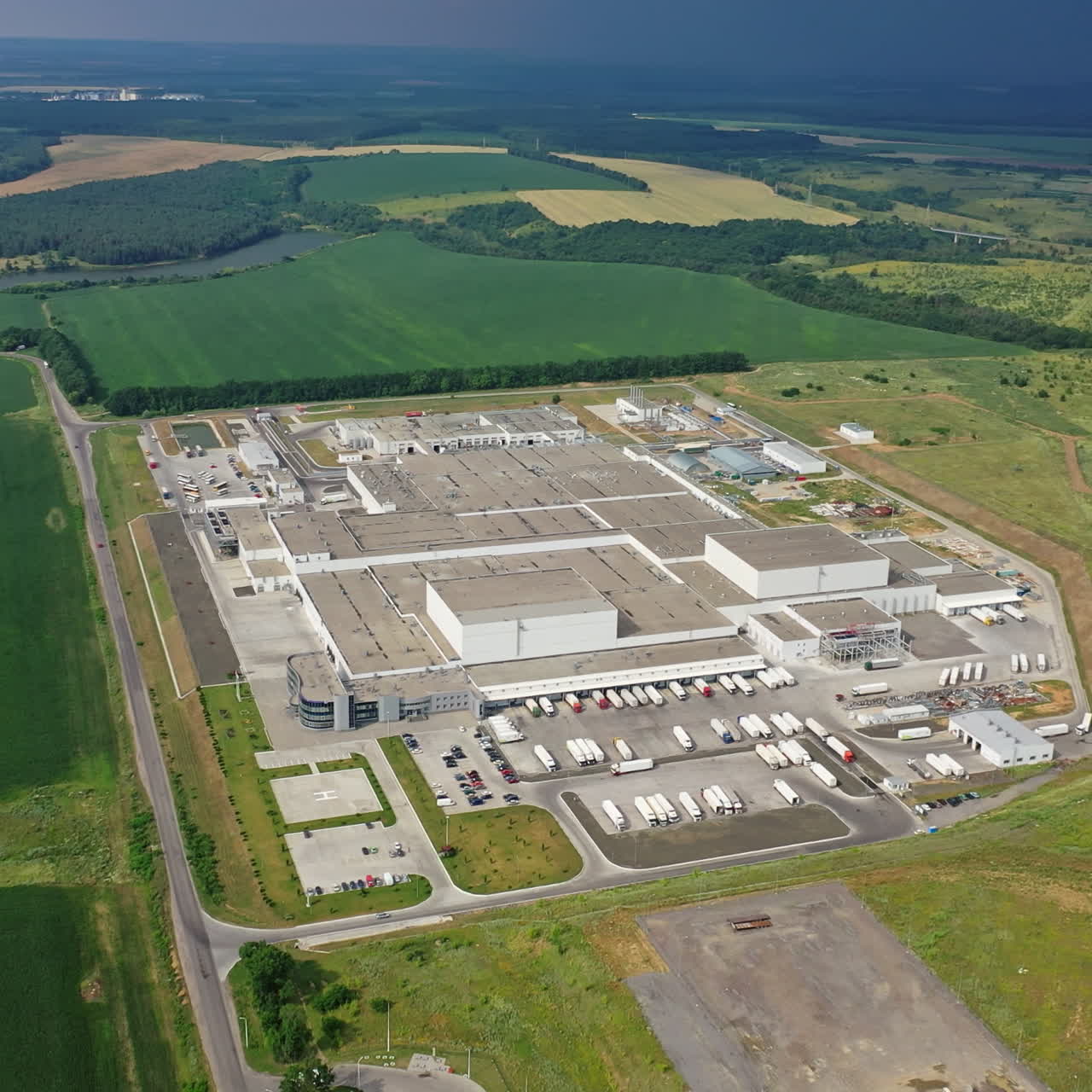 View from above on a huge cargo plant in the midst of nature. Aerial view on roofs of a large industrial complex among green fields.
