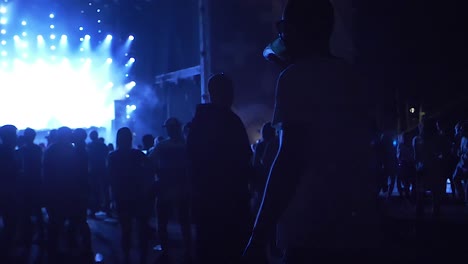 a guy drinking from a plastic cup at the concert, while people are dancing in slow motion