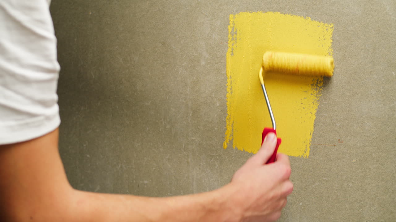 Man's Hand Painting a Wall Yellow with a Roller