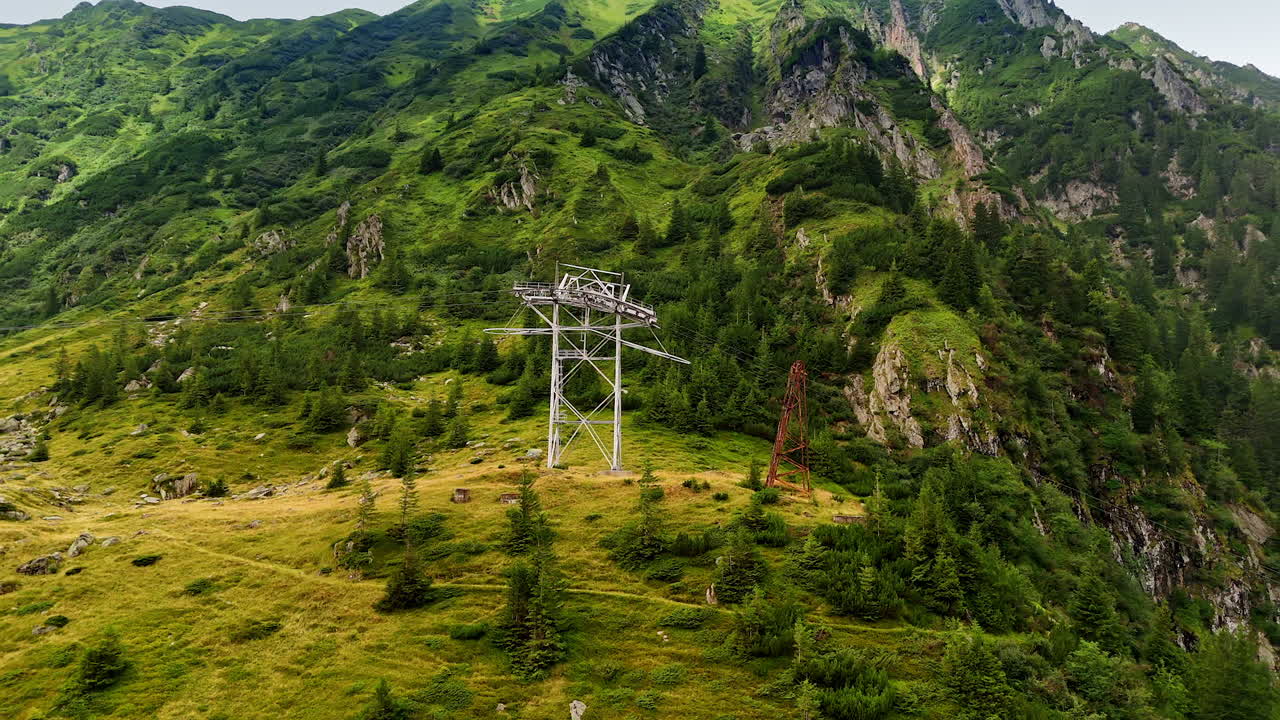 Power line supports installed in the green mountains. Lovely pine trees grow on the slopes. Nature of Romania. Aerial view