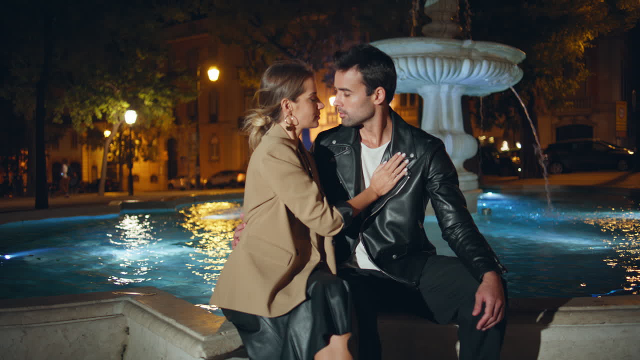 Beautiful woman hugging man gently touch at illuminated city fountain at night
