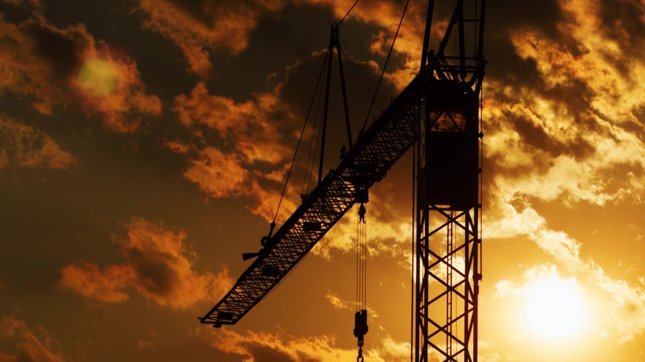 Tower crane appears in silhouette against glowing orange clouds and a bright sunset, showing construction, development and urban growth at dusk.