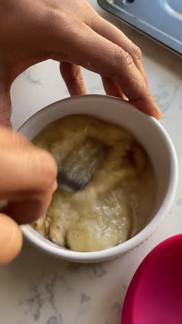 Vertical-video-of-mashing-up-bananas-into-a-small-bowl-to-make-a-batch-of-vegan-donuts