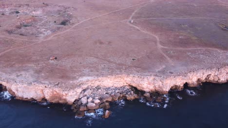 Top-down-aerial-view-of-waves-splash-against-rocky-seashore,-background