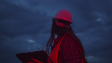 Closeup-portrait-of-woman-engineer-uses-tablet-to-inspect-wind-turbines-at-dusk