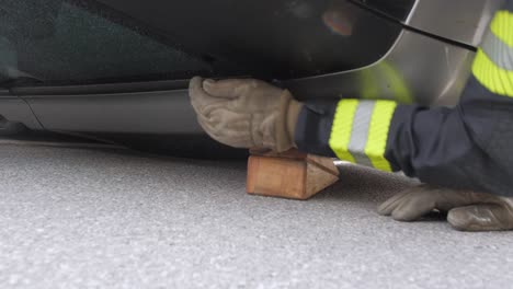 fire fighter puts wooden block under crashed car to stabilize it, closeup