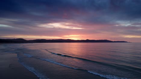 Cielo-De-Puesta-De-Sol-En-Tonos-Con-Reflejo-De-Espejo-En-La-Tranquila-Playa-De-La-Bahía-De-Los-Espíritus,-Isla-Del-Norte,-Nueva-Zelanda