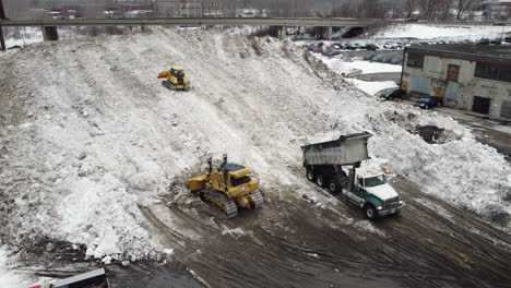 Tractors-with-shovels-clear-snow-under-a-bridge-while-trucks-take-it-away