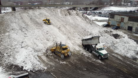 tractors with shovels clear snow under a bridge while trucks take it away