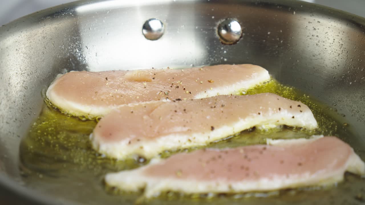주방장이 금속 프라이팬에 닭가슴살을 튀깁니다.