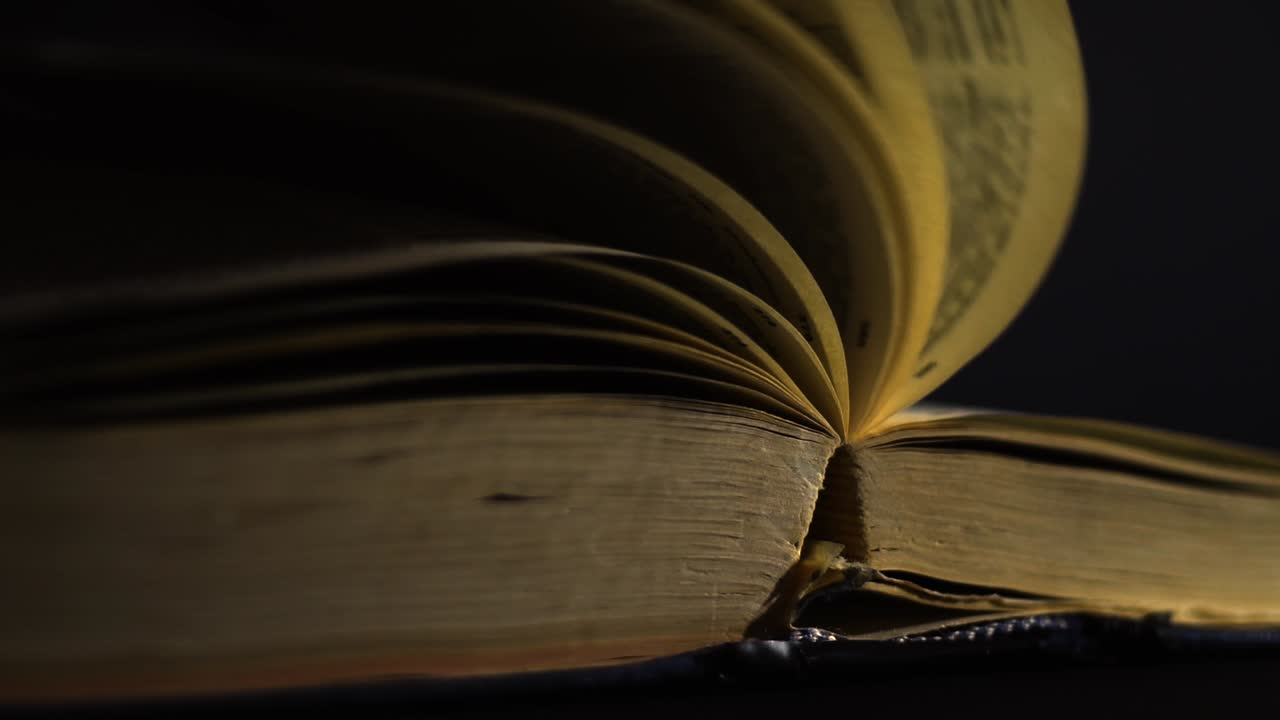 cámara lenta, primer plano de un libro antiguo, vintage, abierto con páginas girando en el viento, en una habitación oscura con poca luz, con un entorno negro