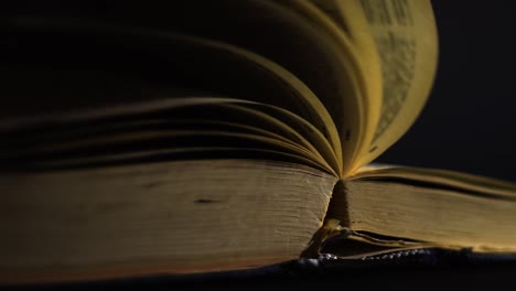cámara lenta, primer plano de un libro antiguo, vintage, abierto con páginas girando en el viento, en una habitación oscura con poca luz, con un entorno negro