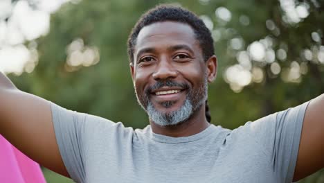 confident middle aged man standing with raised arms, radiating joy and embracing wellness amid lush green park landscape, feeling free and energetic under sunny skies