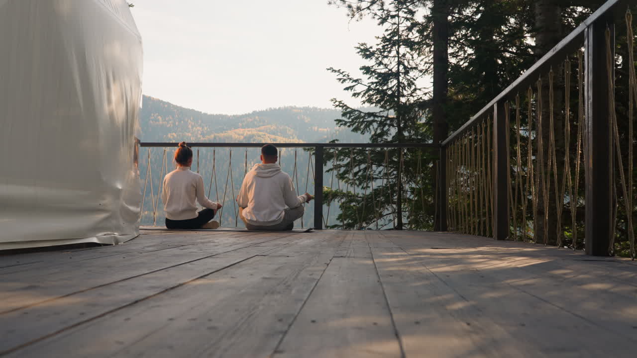 la gente se sienta en posturas de yoga en el piso de madera de la terraza de glamping. la pareja concentrada medita practicando la respiración de yoga para una mente pacífica juntos. estilo de vida saludable