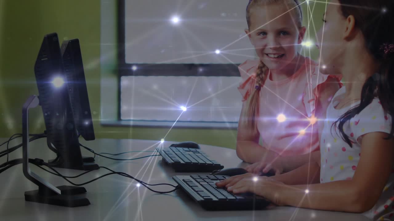 Meninas usando camisas rosa e brancas apontando para o monitor e orientando a digitação em uma área de educação.