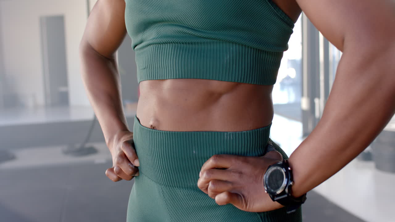 Wearing fitness attire, woman showing toned abs and muscular arms in gym