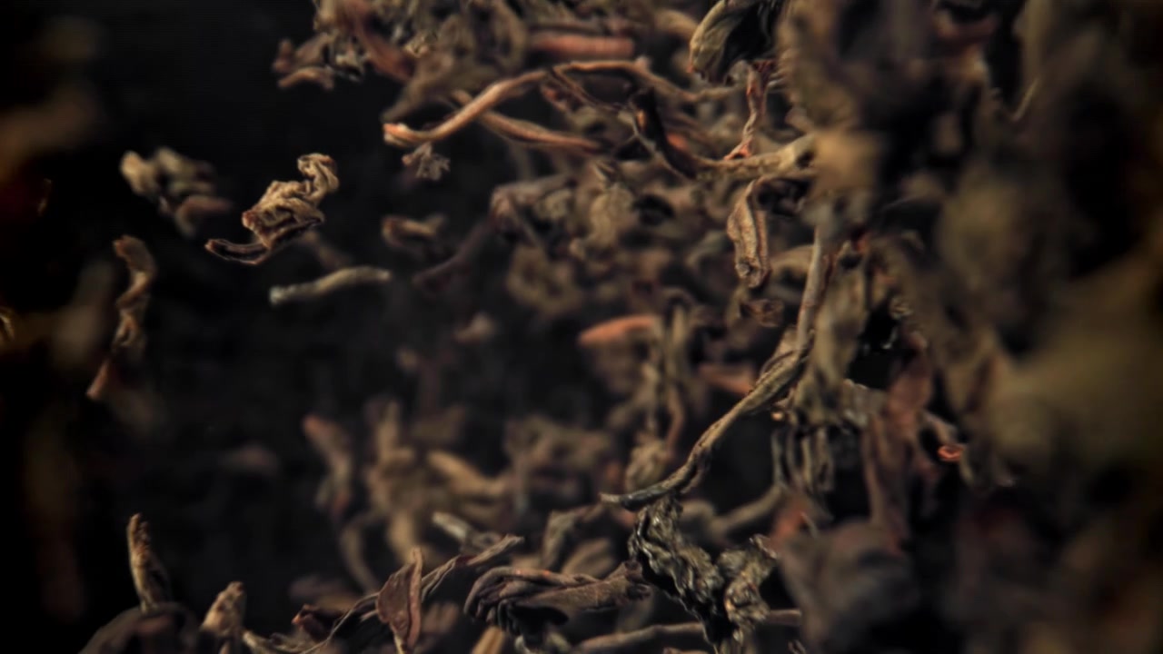 Dried Tea Leaves Falling in Slow Motion on a Dark Background