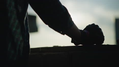 back view of a person wearing a checkered shirt and protective glove, making subtle hand movements against a background with sunlight casting a silhouette effect