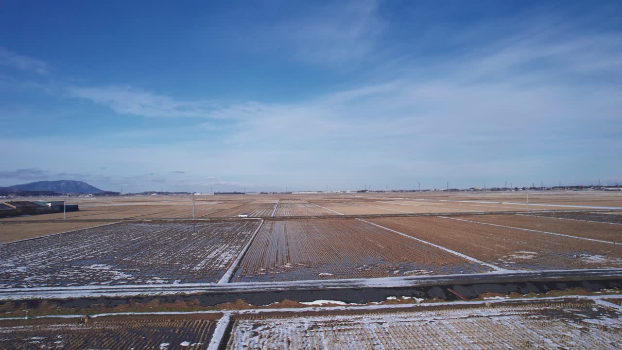 Drone captures winter patterns over Japanese fields with thin layers of frost and distant mountains