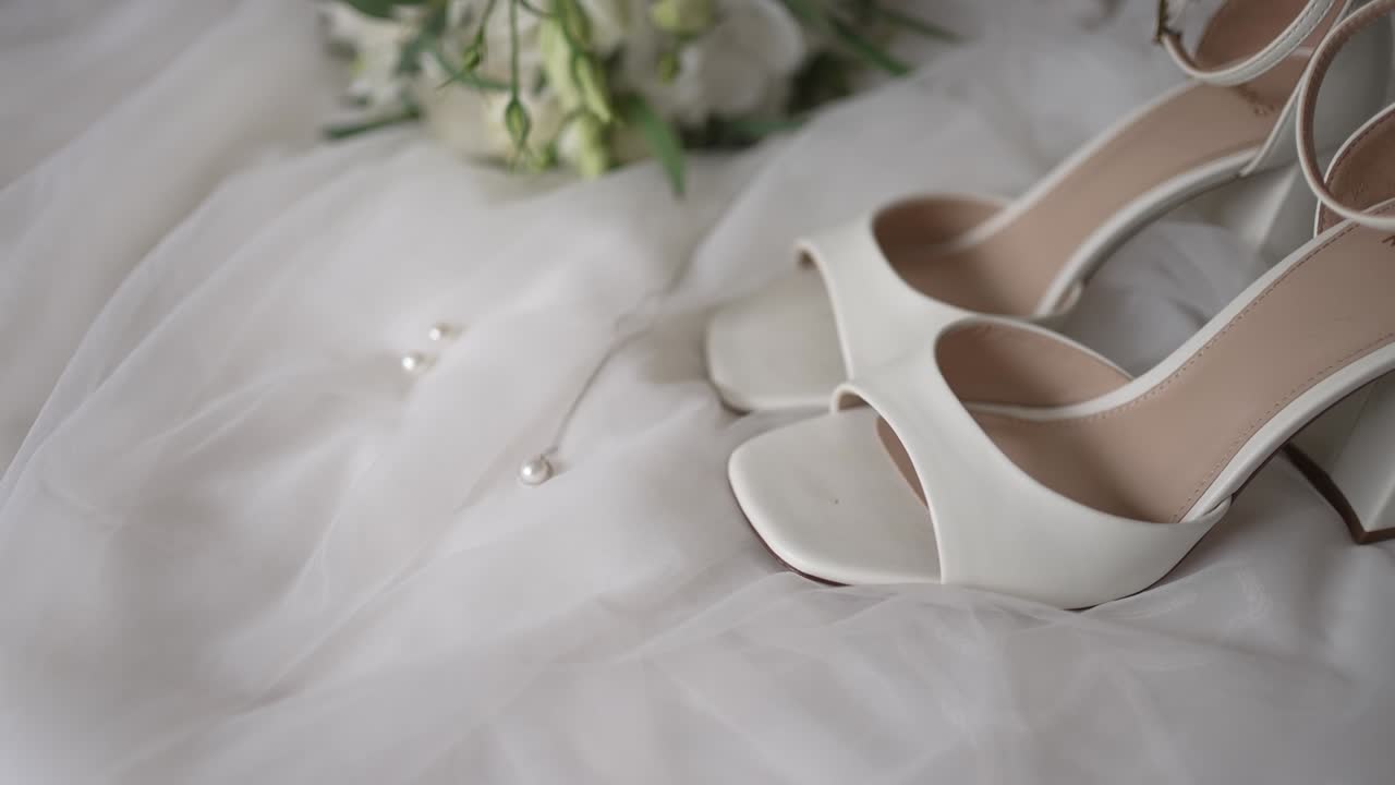 Elegant necklace and dress shoes on satin with flowers and pearls nearby