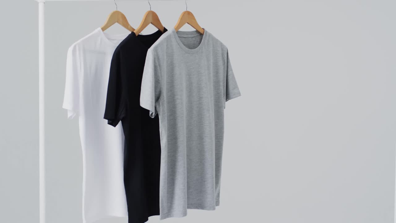 Video of white, grey, black t shirts on hangers and copy space on white background
