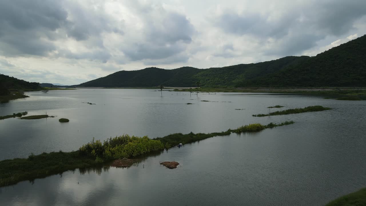 주위에 산이 있는 이 멋진 호수, 비구름이 드리워진 멋진 일몰, 낚시 그물을 치고 있는 물속의 한 남자를 보여주는 공중 하강 영상