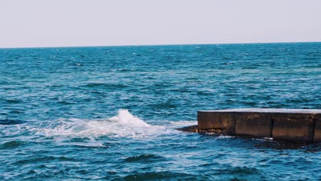 Blue water on the sea surface. Ocean waves crashing against the stone pier. Amazing atmosphere of nature seascape. Slow motion.