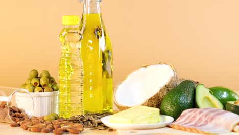 A variety of healthy fats including oils, nuts, and avocados arranged on a wooden table with warm lighting