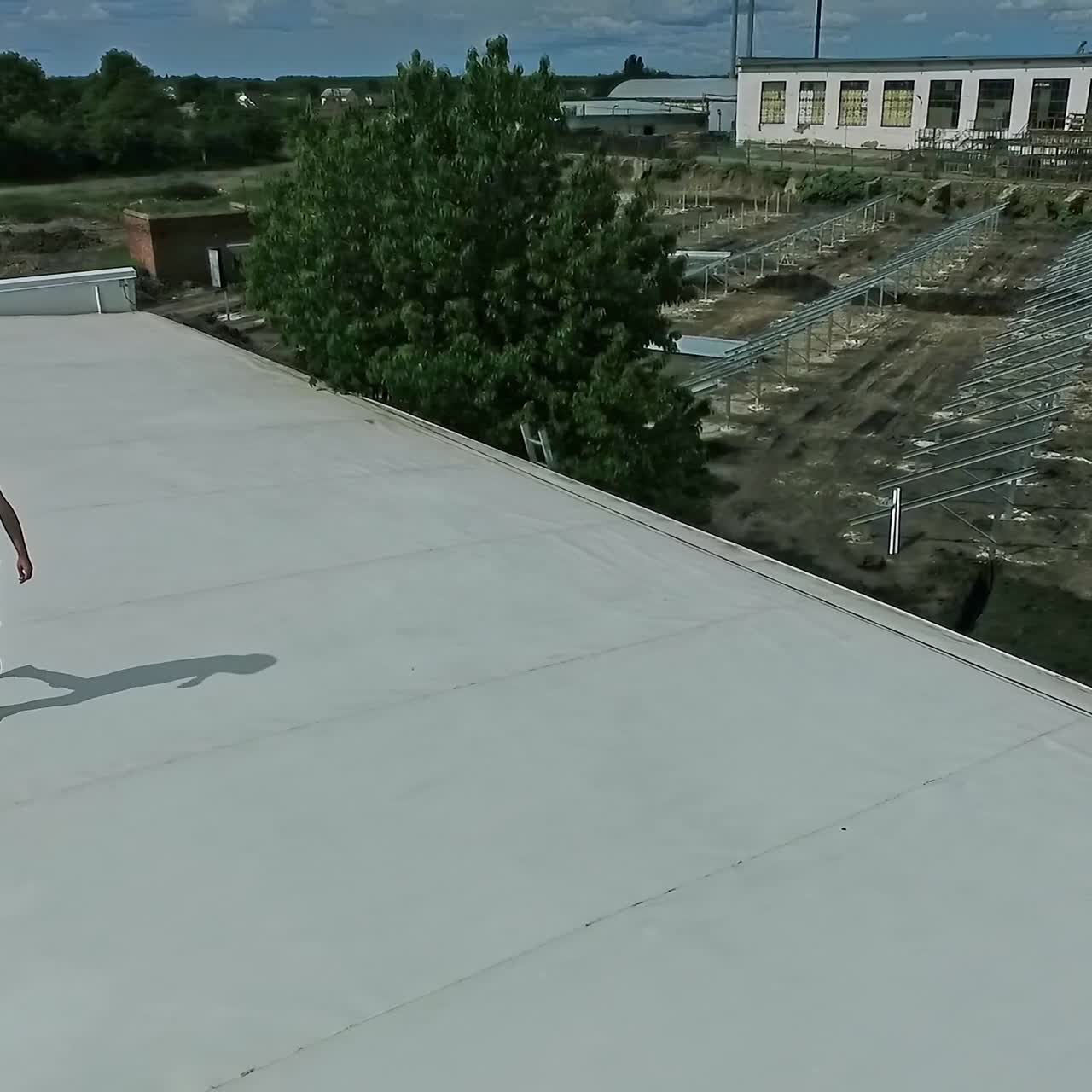 Technical expert walking on flat roof of a building. Male worker in orange protective hard hat on a roof top develops the plan of construction of solar farm.