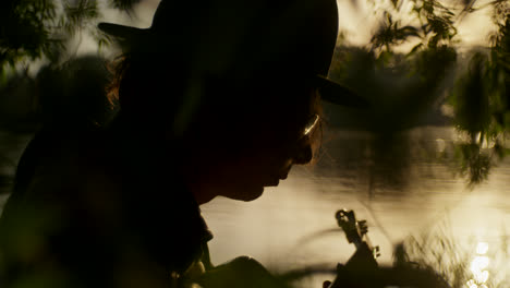 silhouette of musician playing guitar by a river at sunset