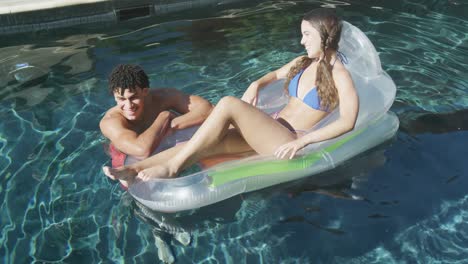 Happy-biracial-couple-with-inflatable-in-swimming-pool-on-sunny-day