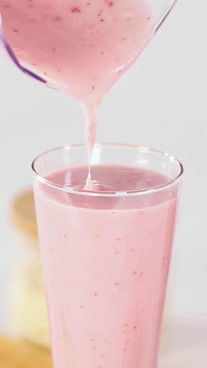 Batido cremoso de fresa rosa vertido en un vaso transparente, primer plano, iluminación brillante, fondo minimalista.