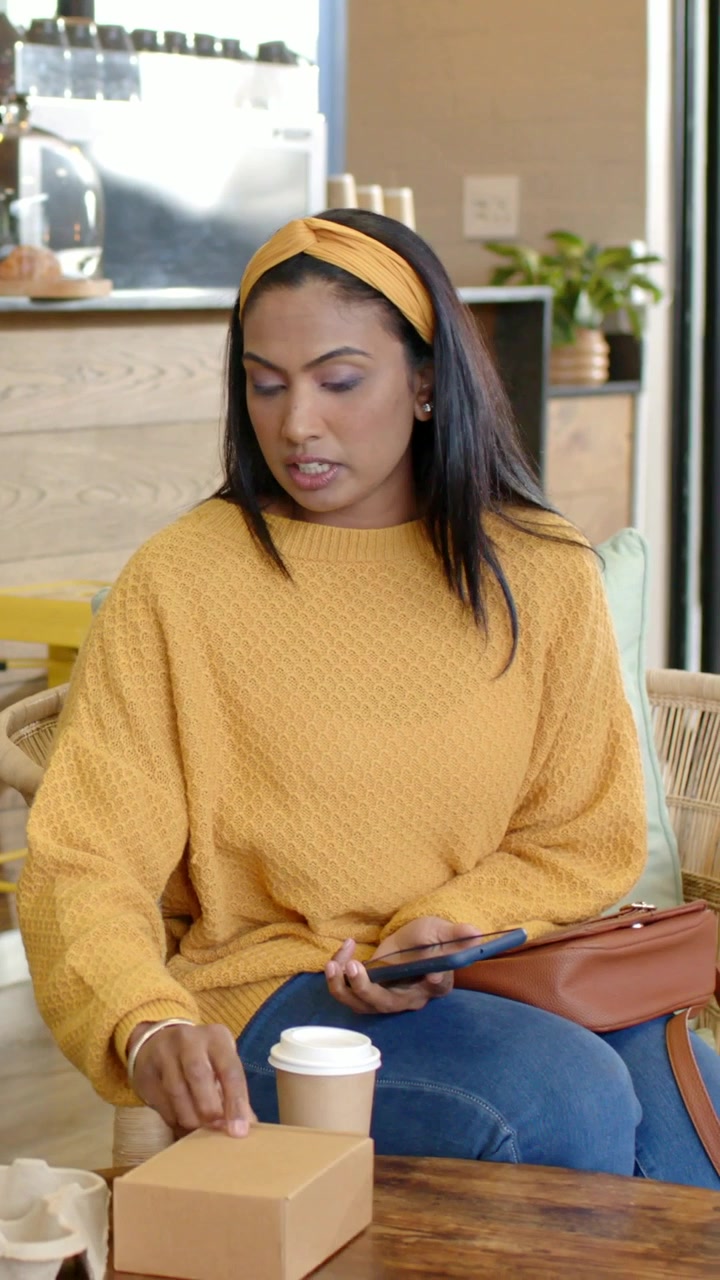 Vertical video: Handing cup woman in yellow top taking coffee moving box and checking phone at cafe