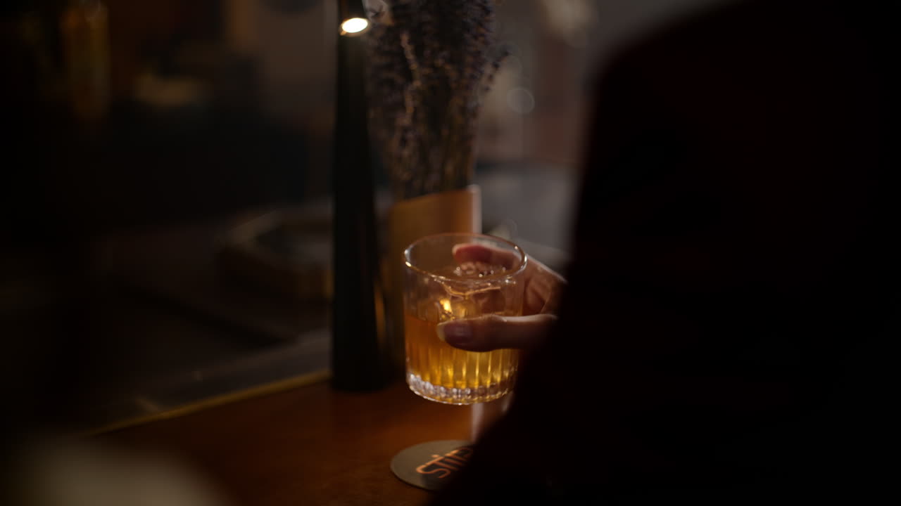 Contemplative person holding a drink, looking pensively in a cozy bar setting