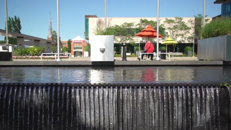 sidetracking shot of a waterfall over a wall at whitby public library square with modern architecture in the background