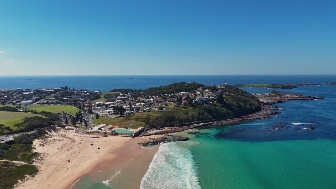 Port Kembla coastline showing beach, headlands and turquoise waters under clear sky, panoramic aerial, Sydney NSW Australia