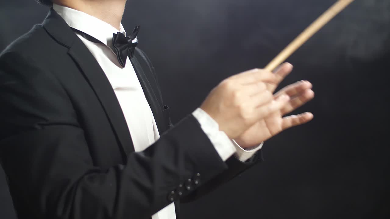 안개가 가득한 검은 스튜디오에서 눈을 감고 몸짓을 보이는 아시아계 지휘자 남자.