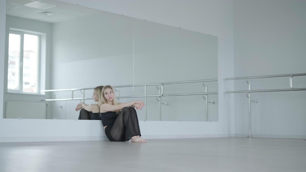 Fit girl in black clothes performing contemporary. Female dancer shows flowing motions, body and hands waves at white room. Modern ballet dance choreography. Young woman is moving smoothly