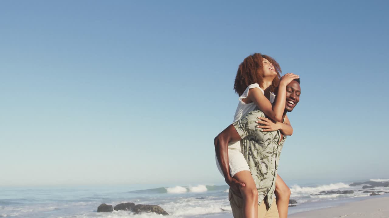African American man carrying his wife on his back at beach