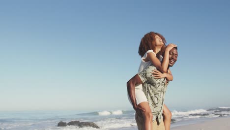 african american man carrying his wife on his back at beach