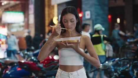 woman eating noodles on a night street