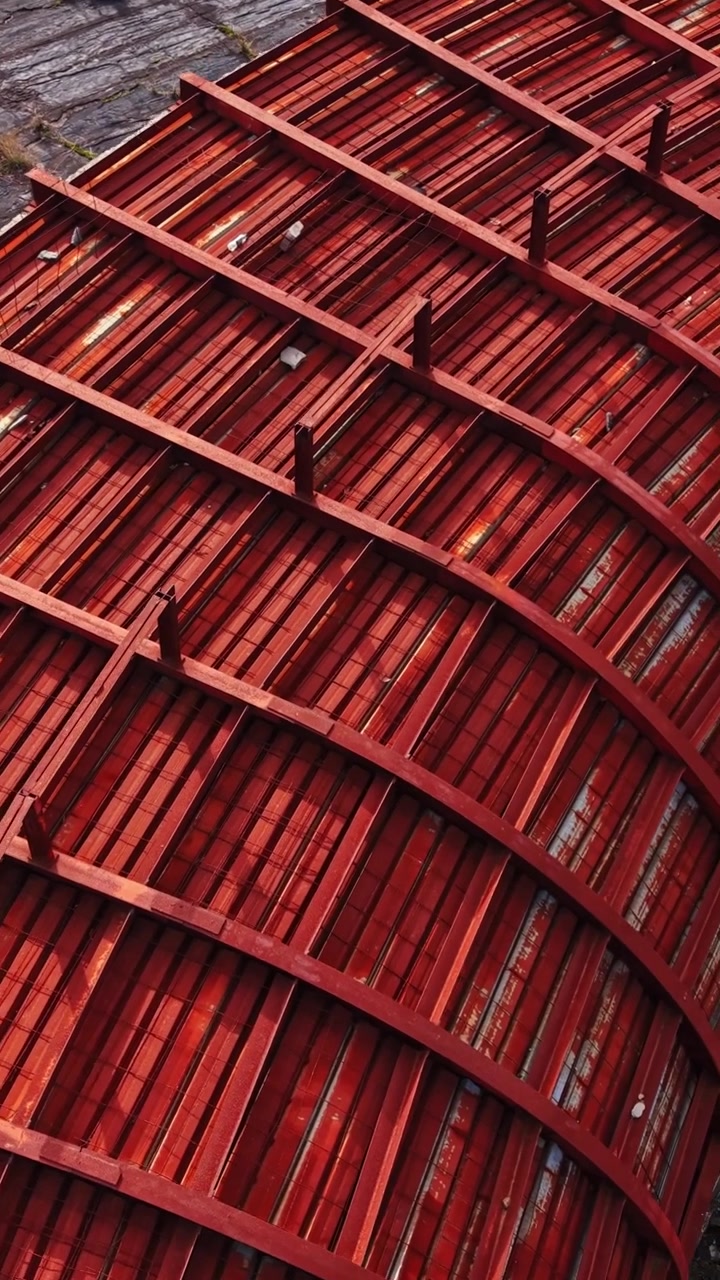 Vue aérienne d’une structure rouge incurvée avec du bois patiné et un environnement verdoyant