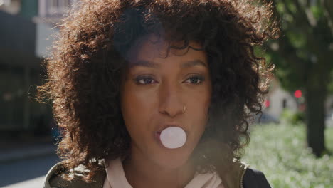 retrato en primer plano de una joven mujer afroamericana soplando chicle sonriendo feliz disfrutando de una diversión juguetona en la soleada calle de la ciudad por la mañana estudiante con peinado afro