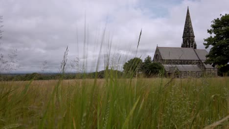 UK-church-and-steeple-through-hayfield-in-village-and-tree-lined