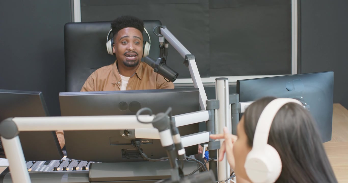 Diverse hosts reacting to cue, African American man adjusting console, woman reading notes into mic