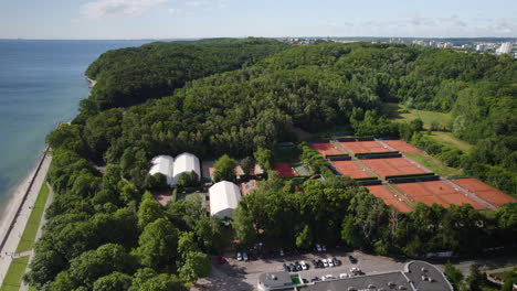 aerial view of seaside boulevard area in gdynia city poland, tennis outdoor clay courts surrounded by beautiful nature forest topped lands and hills along the seashore, coastal landscape