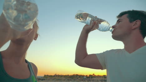 two people drinking water from plastic bottles