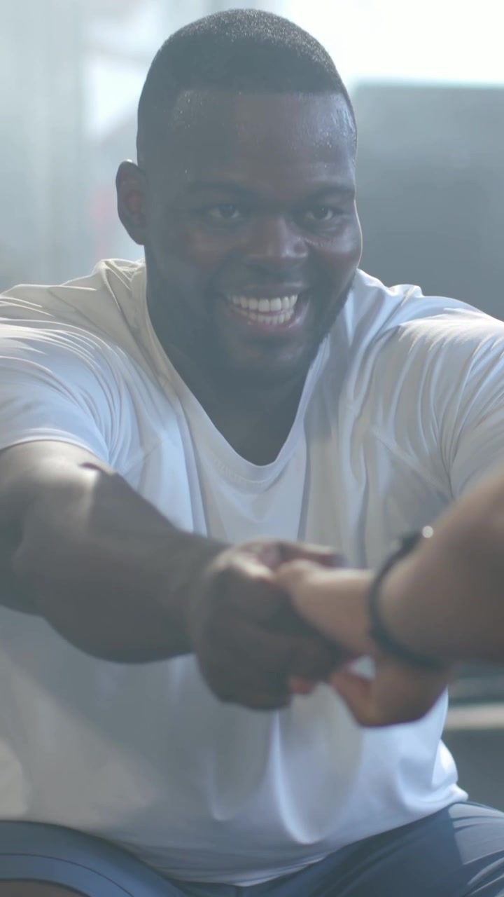 Vertical video: Partner offering hands, man in white tee gripping hands in gym for workout band