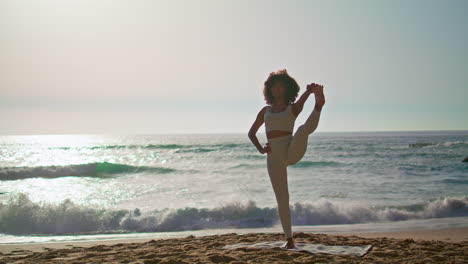 mujer practicando el equilibrio de la postura en la playa al amanecer. niña de pie en una pierna.